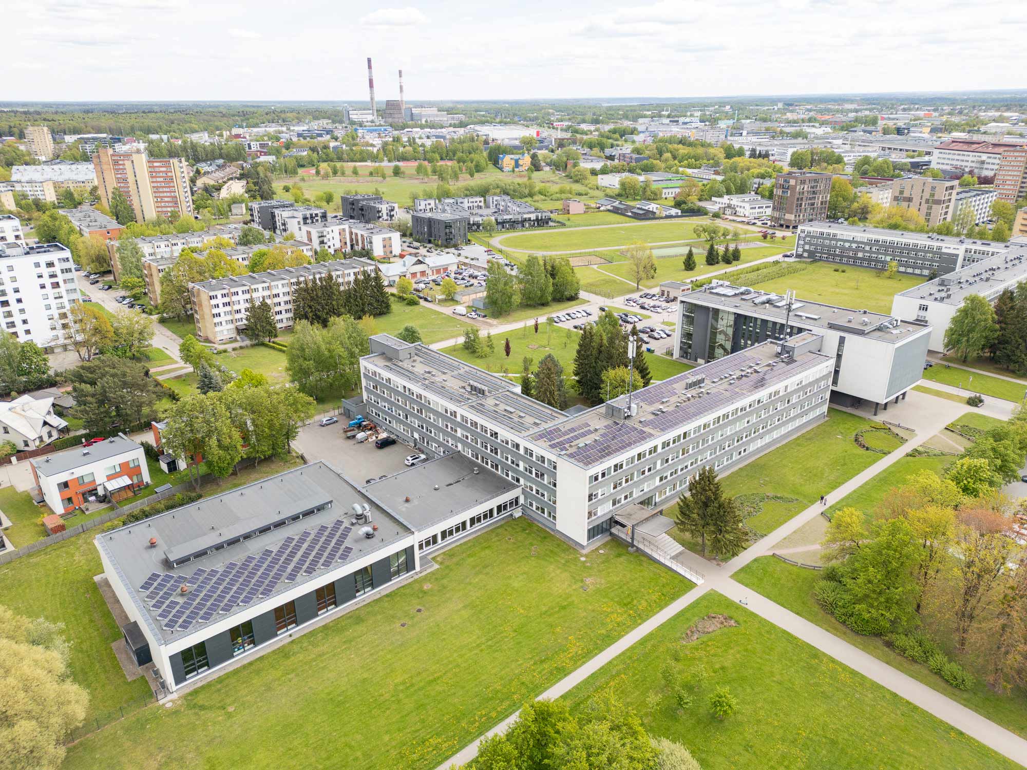 Aerial view of the Kauno Kolegija campus buildings with rooftop solar panels surrounded by green lawns and the city.