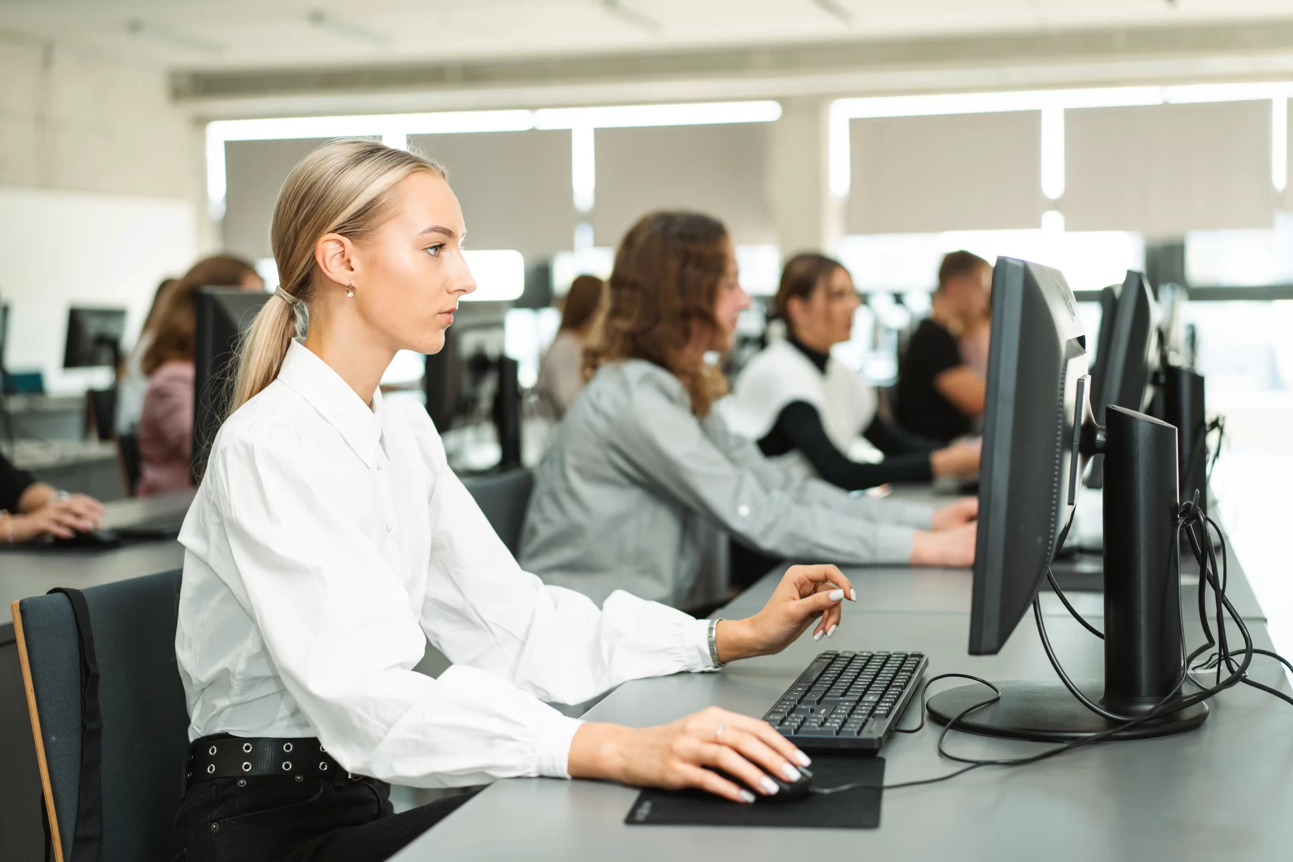Focused female student working at a desktop computer in a modern university computer lab.