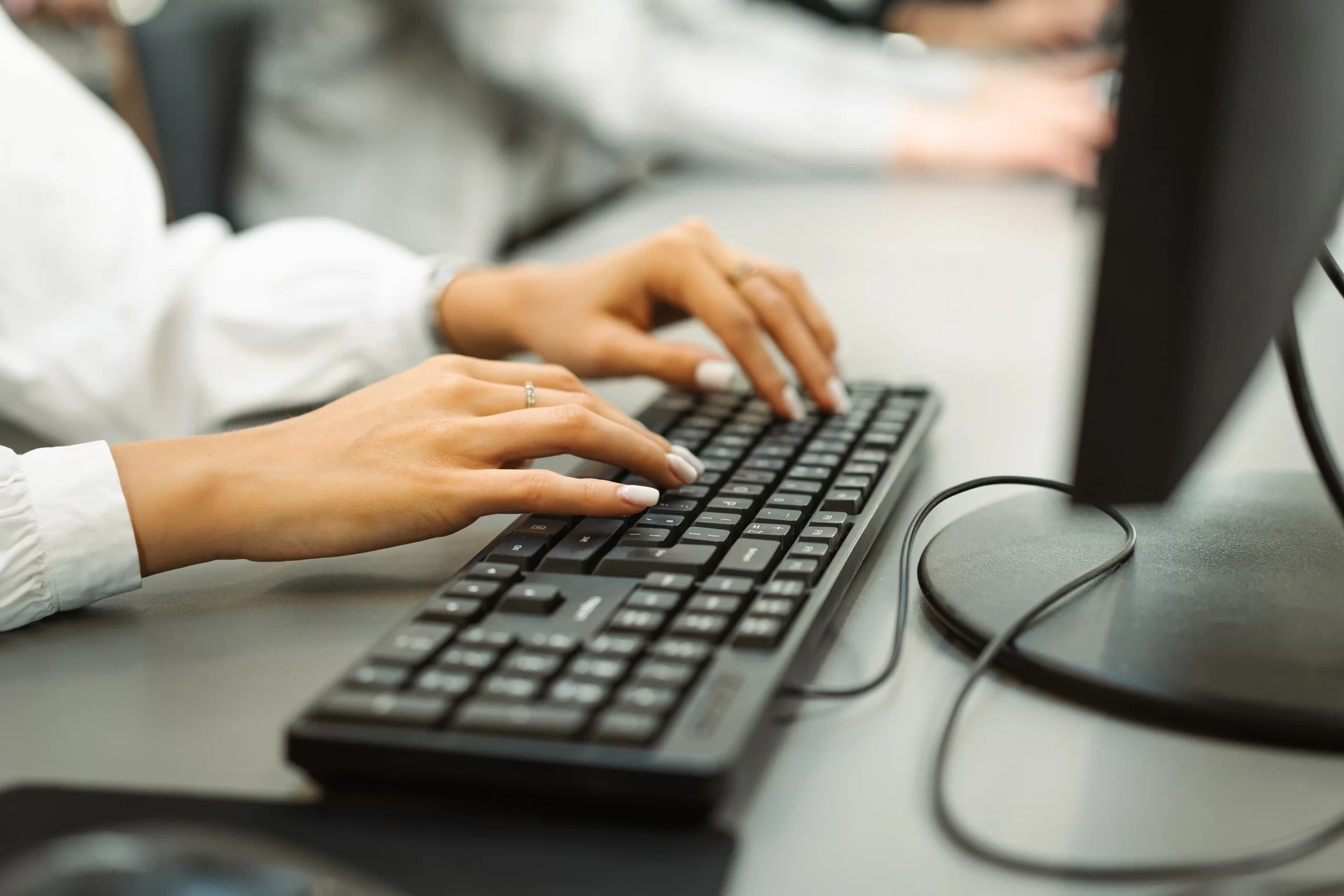 Close-up of a female student's hands typing on a black desktop computer keyboard.