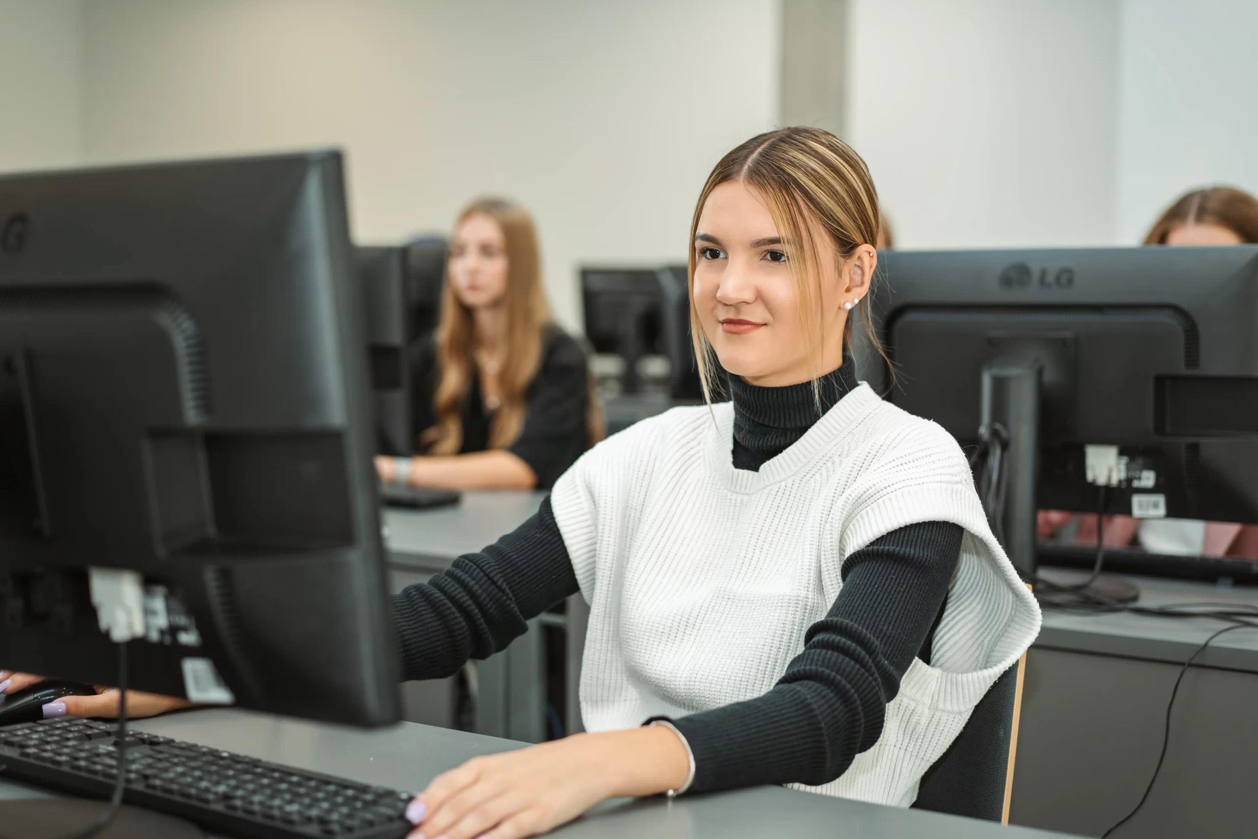 Smiling female student working at a desktop computer in a modern college computer lab.