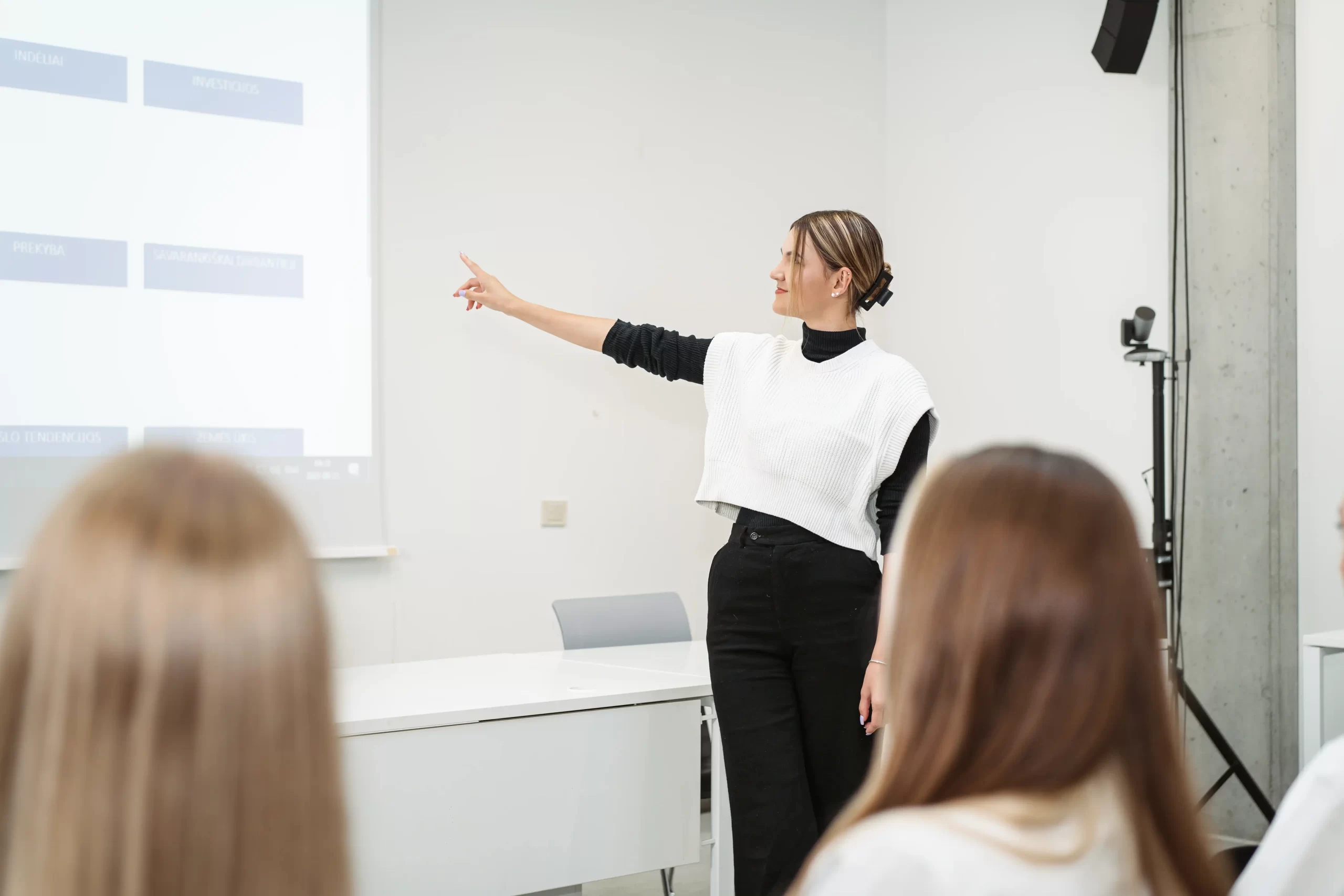 Female student giving a presentation and pointing at a chart on a projection screen in a classroom.