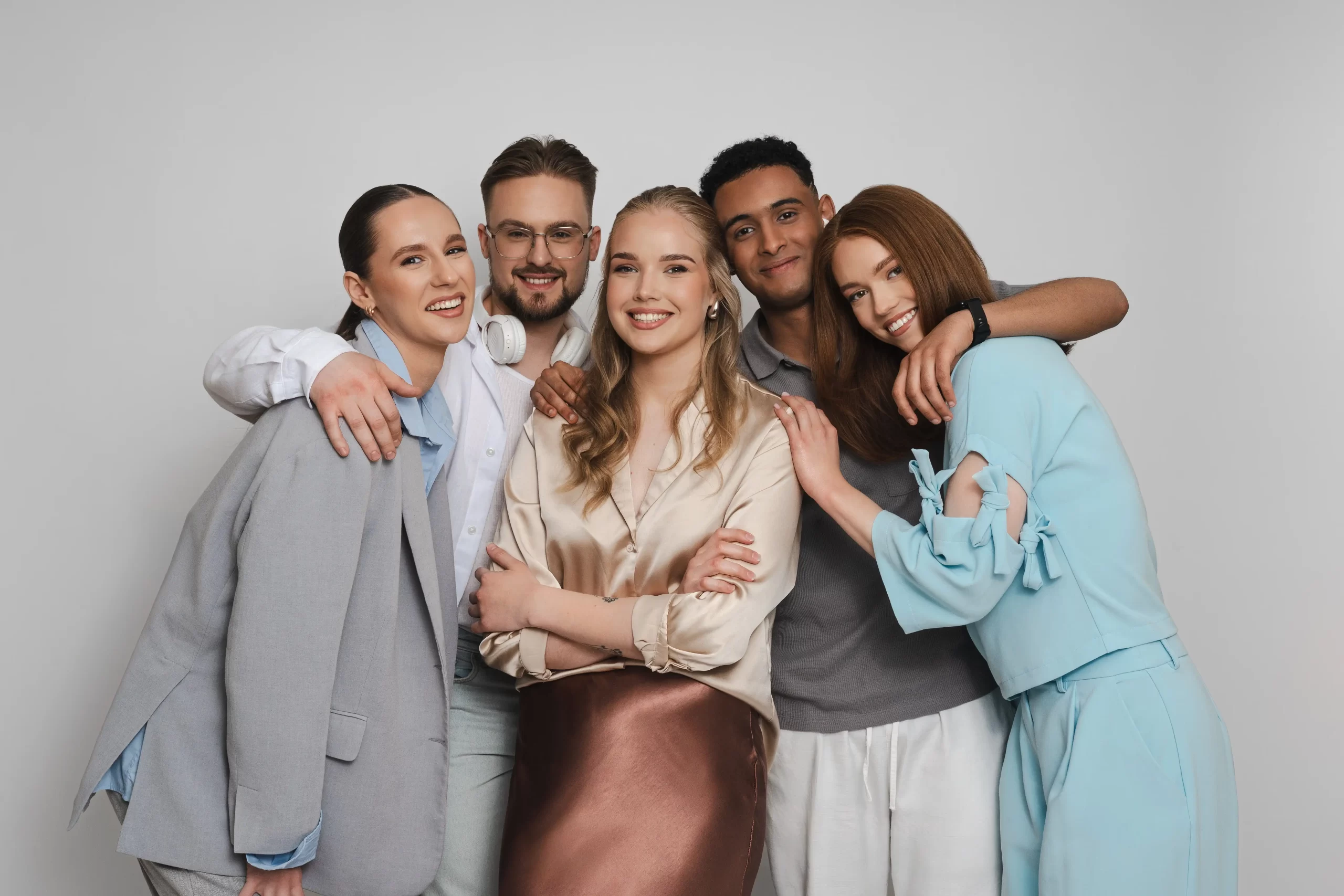 Happy diverse group of five students embracing and smiling at the camera.