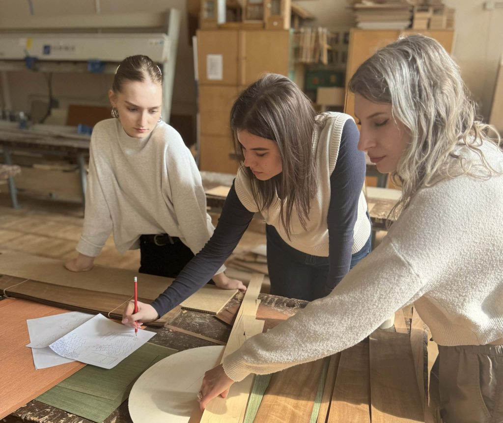 Students working with wood samples and design sketches during a conservation and restoration study session in a workshop.