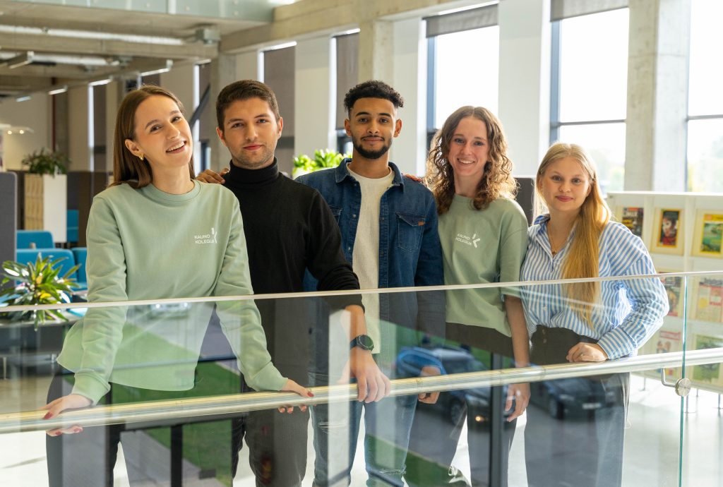 Five diverse students from Kauno kolegija posing together in a bright, modern building