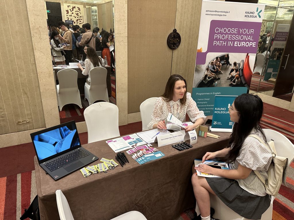 Representative from Kauno kolegija speaks with a prospective student at an international education fair in Vietnam, presenting study programmes and materials at an information booth.