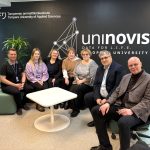 Group of representatives from Kauno kolegija and Tampere University of Applied Sciences (TAMK) seated together in a modern campus space, posing in front of a UNINOVIS wall during a partnership visit.