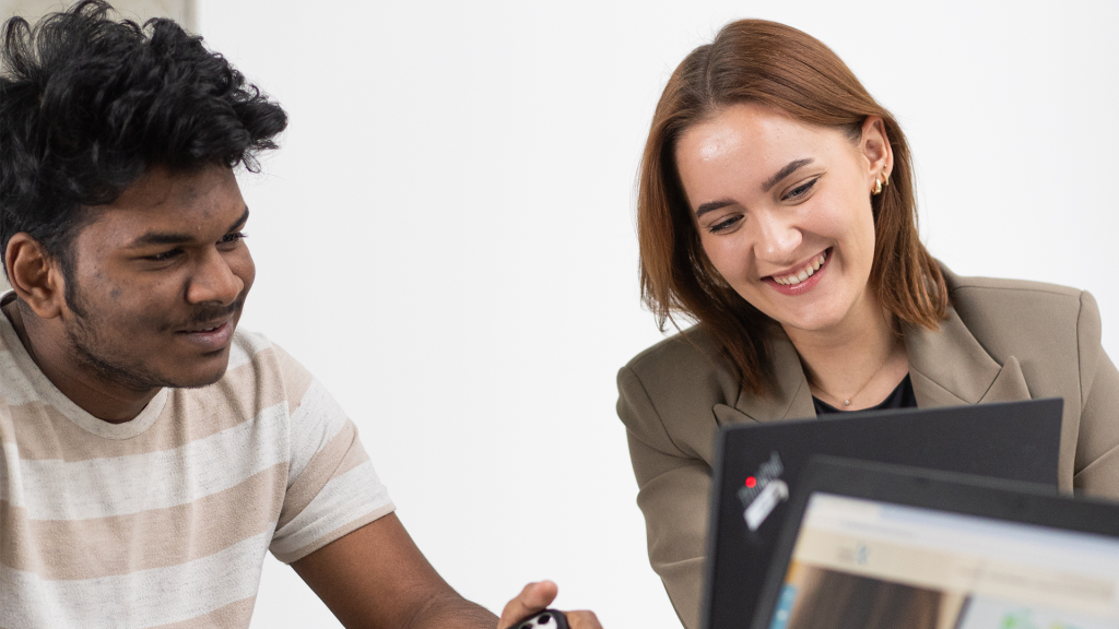 Two students collaborating at a laptop, smiling and discussing ideas during a study session.