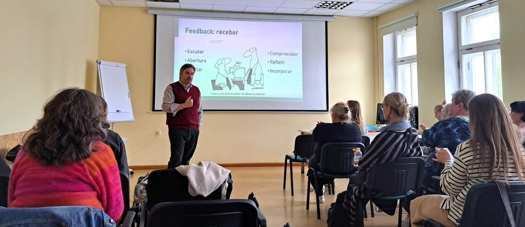 A lecturer giving a presentation to students in a classroom during an international academic visit, with a slide about feedback and communication skills displayed on the screen.