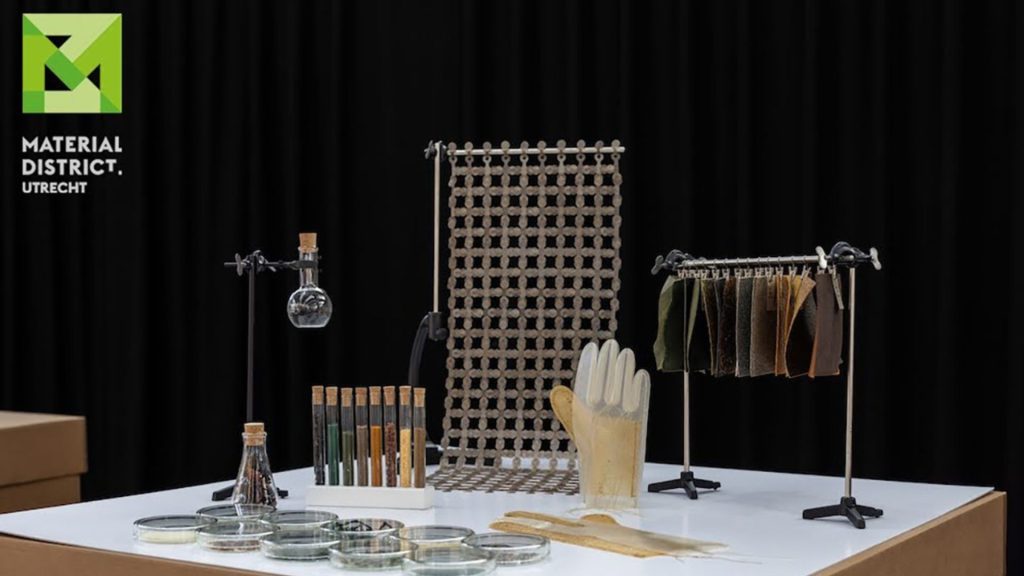 Biomaterials exhibition at the international platform “MaterialDistrict Utrecht 2026”, featuring laboratory glassware, biomaterial samples, textile swatches, and gloves made from biomaterials.