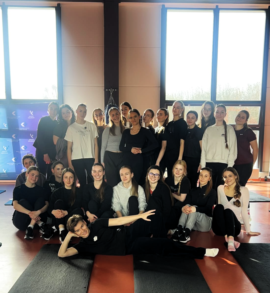 Odontologinės priežiūros studijų programos studentai po praktinio užsiėmimo apie ergonomiką odontologijoje bendroje nuotraukoje su sveikatingumo specialiste sporto salėje.