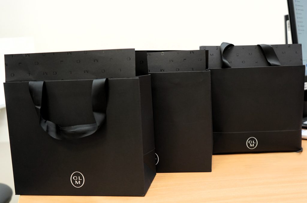 Ant stalo sustatyti trys juodi „CLM“ dovanų maišeliai su juodomis rankenomis skirti apdovanoti konkurso nugalėtojus.