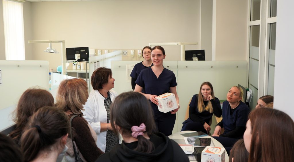 Burnos sveikatos edukacija Kauno kolegijos Medicinos fakultete – studentė pristato danties sandaros modelį ir pasakoja gimnazistams apie burnos priežiūrą praktinio užsiėmimo metu.