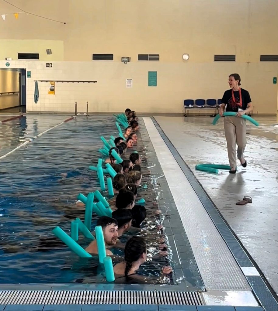 Praktinis užsiėmimas baseine, kuriame dalyviai atlieka veiklas vandenyje su plūdrumo priemonėmis