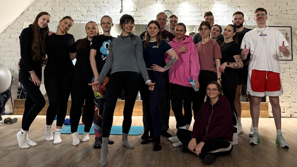 Kineziterapijos alumnai ir studentai po praktinio užsiėmimo sporto salėje pozuoja bendrai nuotraukai.