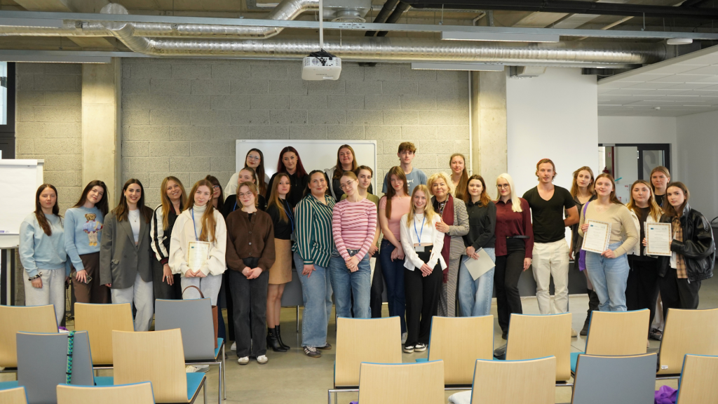 BIP „Wellbeing from Nature“ programos dalyviai stovi grupinėje nuotraukoje Kauno kolegijos auditorijoje. Nuotraukoje matomi studentai ir dėstytojai, dalis jų rankose laiko įteiktus sertifikatus.