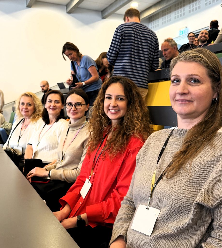 Konferencijos dalyvės sėdi auditorijoje ir dalyvauja tarptautinio renginio veiklose.