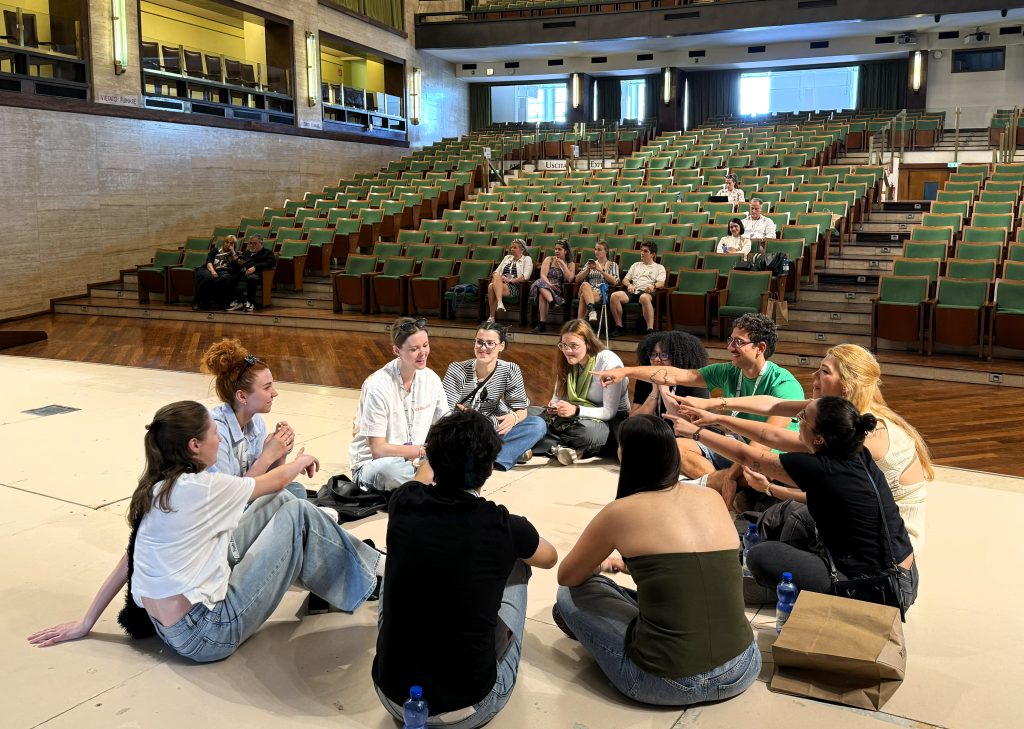 Susitikimas Romos Sapienza universitete: studentai sėdi ratu auditorijos scenoje ir dalyvauja interaktyvioje diskusijoje.