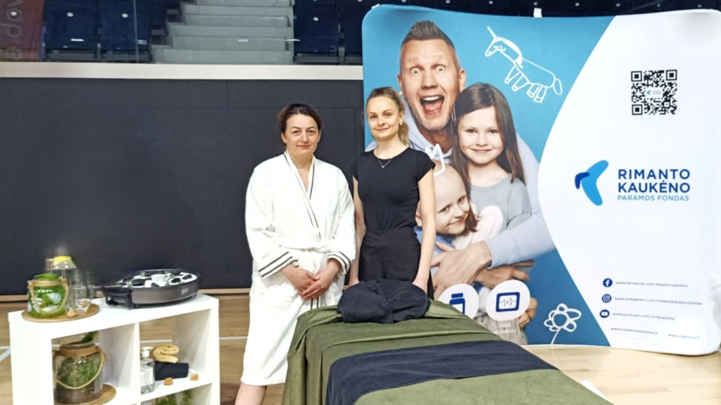 Kauno kolegijos studentė ir dėstytoja tarptautiniame masažo čempionate prie masažo stalo ir Rimanto Kaukėno paramos fondo stendo.