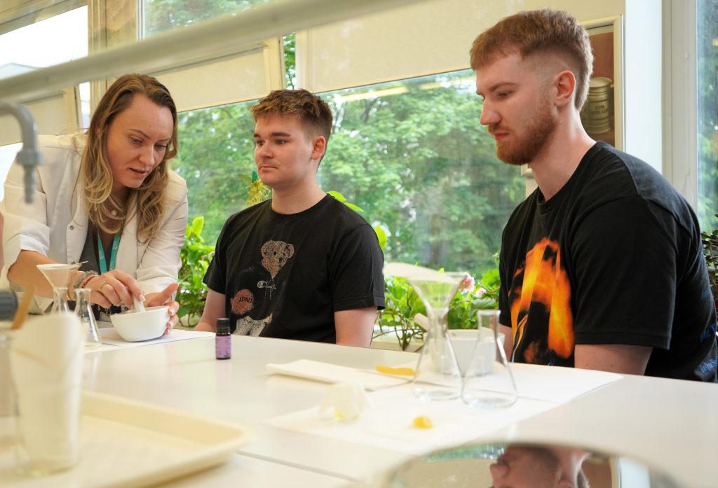 Erasmus+ BIP savaitės „Holistic Natural Cosmetics“ dalyviai laboratorijoje stebi natūralios kosmetikos gamybos procesą.