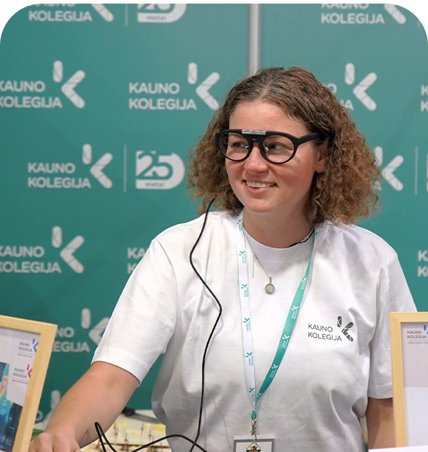 Besišypsanti atstovė su išmaniaisiais akiniais stovi prie stendo su užrašais „Kauno kolegija“ ir „25 metai“.