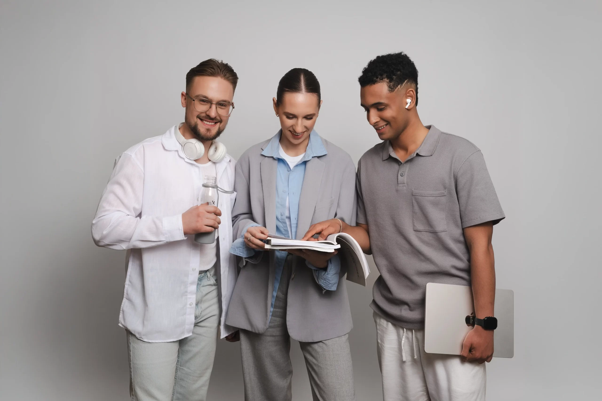 Besišypsantys studentai su nešiojamuoju kompiuteriu ir ausinėmis kartu nagrinėja atverstą knygą.