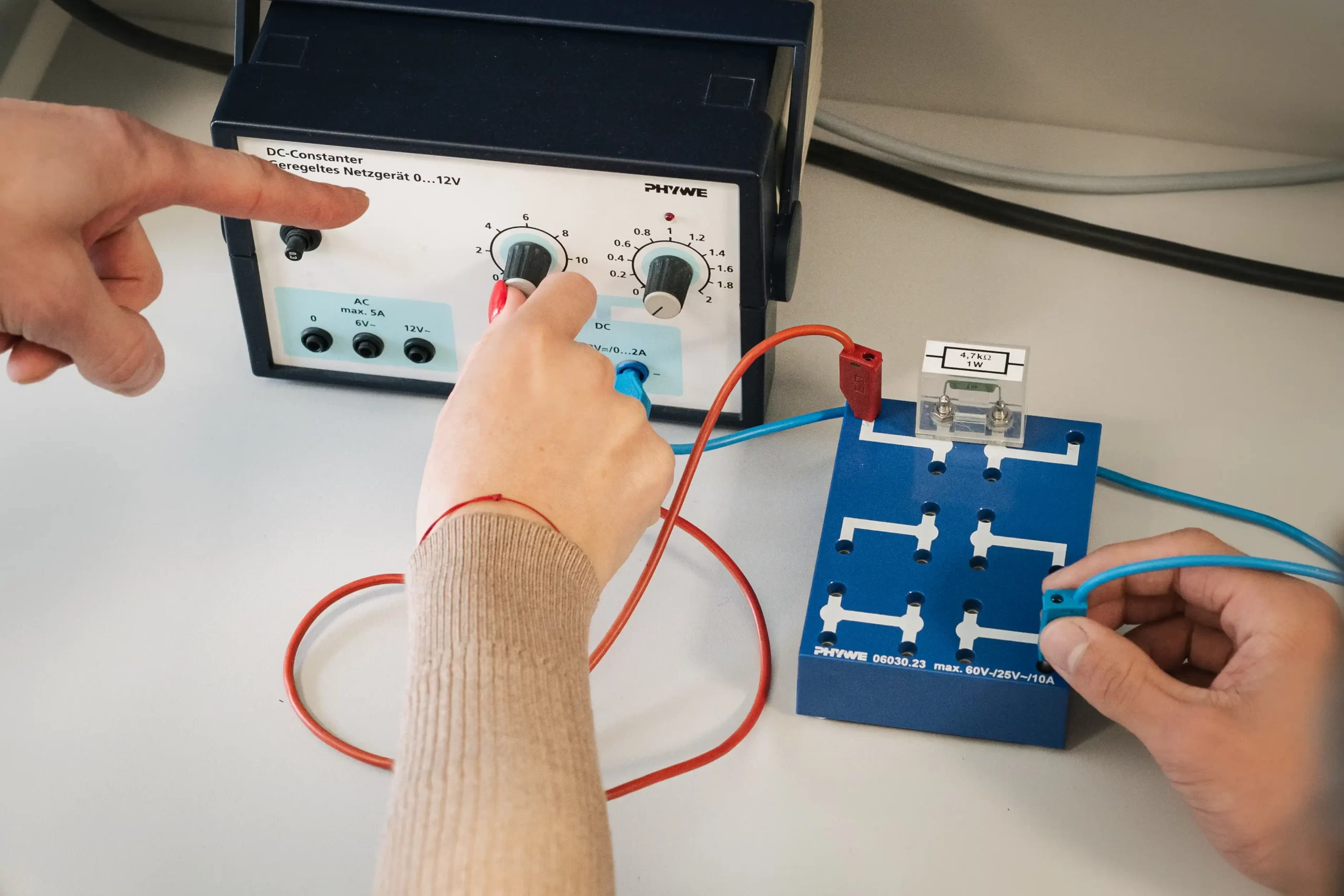 Studentai fizikos laboratorijoje reguliuoja maitinimo šaltinį ir jungia elektros grandinę.