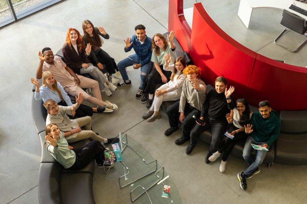 Besišypsantys ir mojuojantys Kauno kolegijos studentai modernioje aukštosios mokyklos aplinkoje.